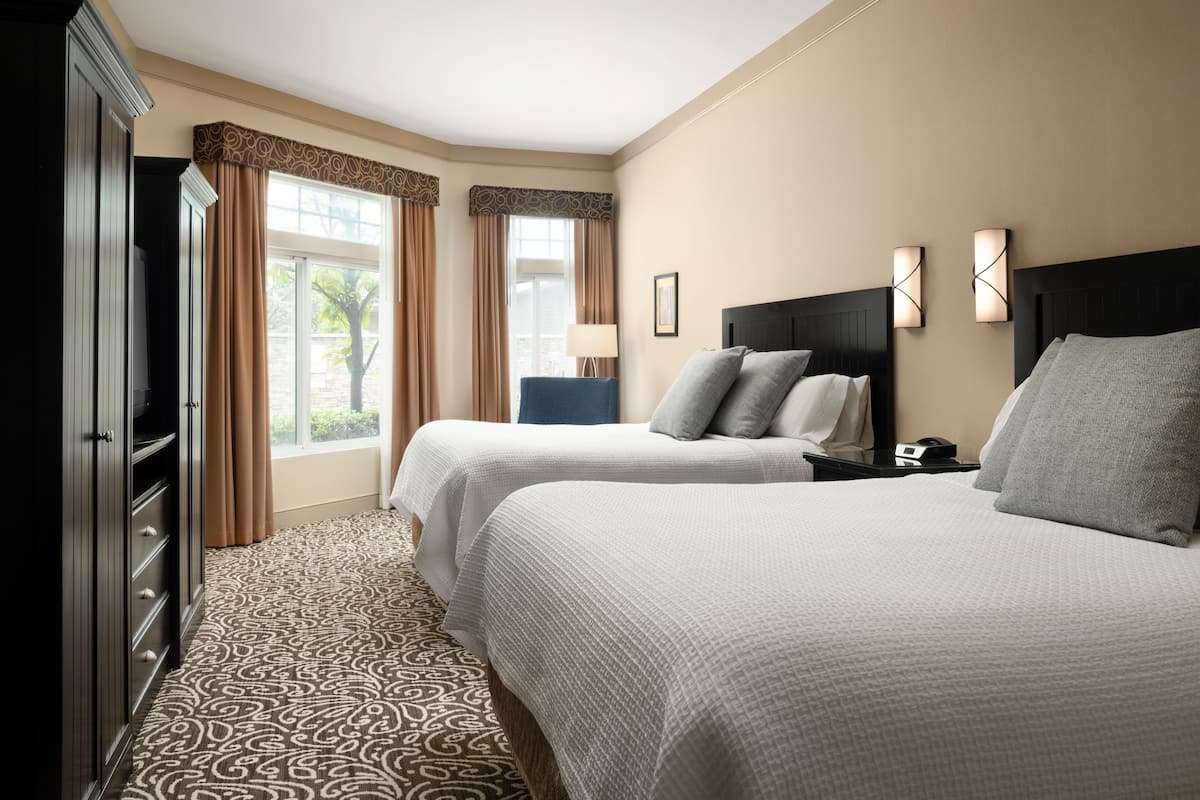 A hotel room with two beds, a wardrobe, a desk, and a window with curtains.