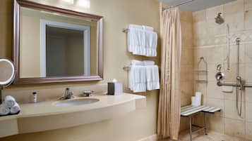 Un baño moderno con un espejo grande, un lavamanos, una ducha y varias toallas.