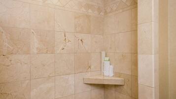 A shower area with beige tiles, a shelf with toiletries, and a drain.