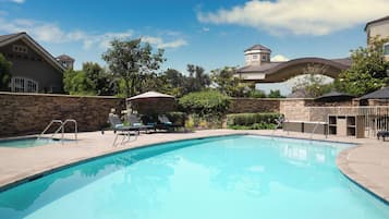 A swimming pool with lounge chairs and umbrellas, surrounded by stone walls and greenery.