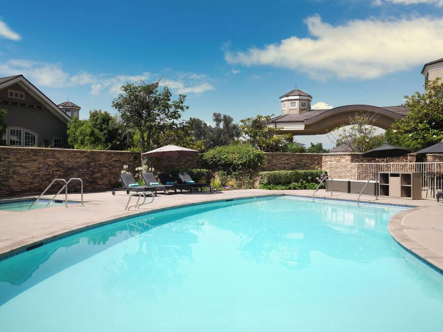 A swimming pool with lounge chairs and umbrellas, surrounded by stone walls and greenery.