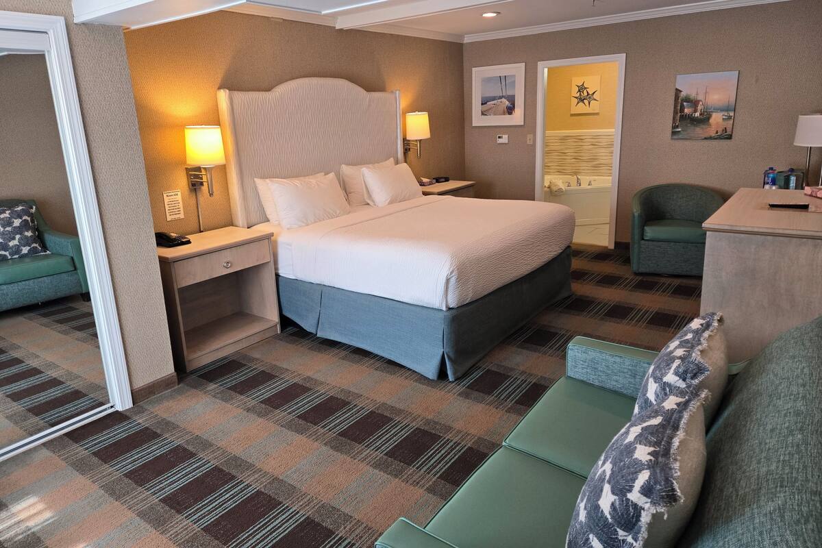 A hotel room with a large bed, a green armchair, a small desk, and a bathroom visible through an open door.