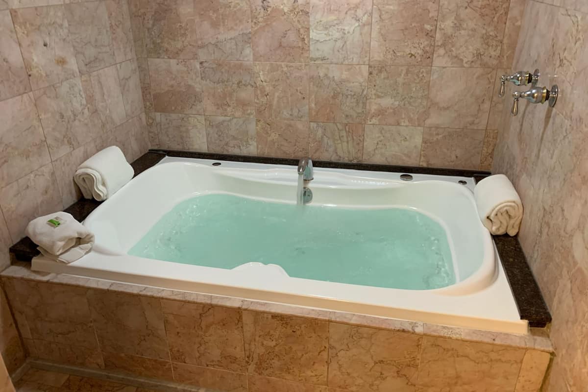 A rectangular bathtub with a faucet, two towels, and a green bottle on the side.