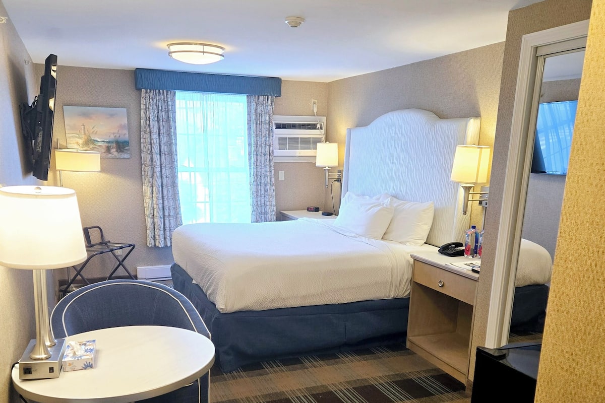 A hotel room with a bed, a desk, a chair, a lamp, and a television.
