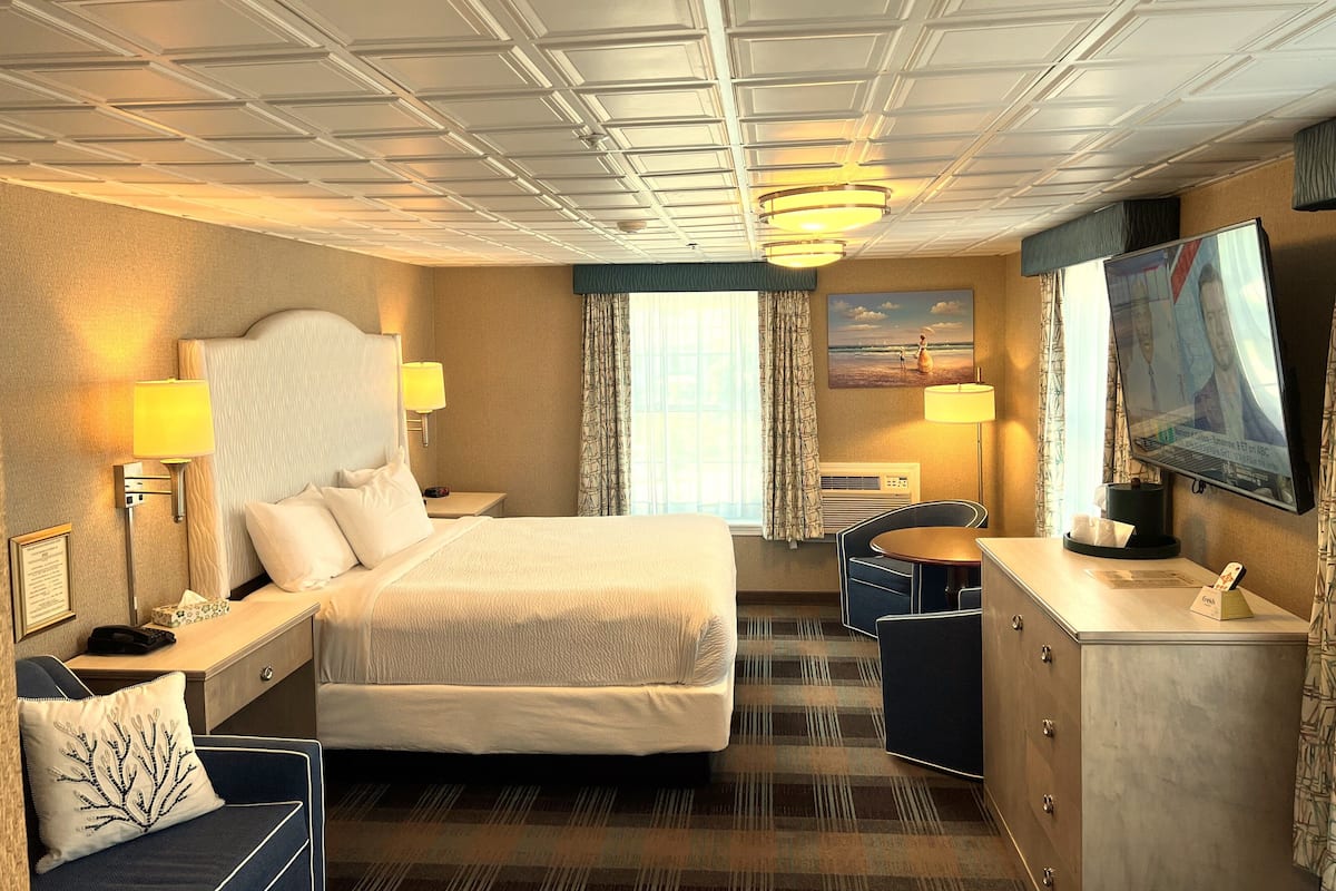 A hotel room with a bed, bedside lamps, a desk, a chair, a television, and a window with curtains.