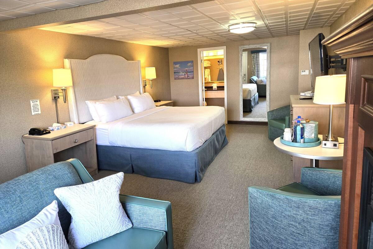 A hotel room with a bed, two bedside tables, a desk with a chair, a sofa, and a mirror.