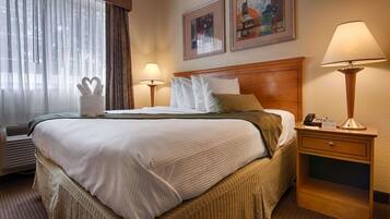 Une chambre d’hôtel avec un grand lit, deux lampes de chevet, une table de chevet avec un téléphone et une fenêtre avec des rideaux.