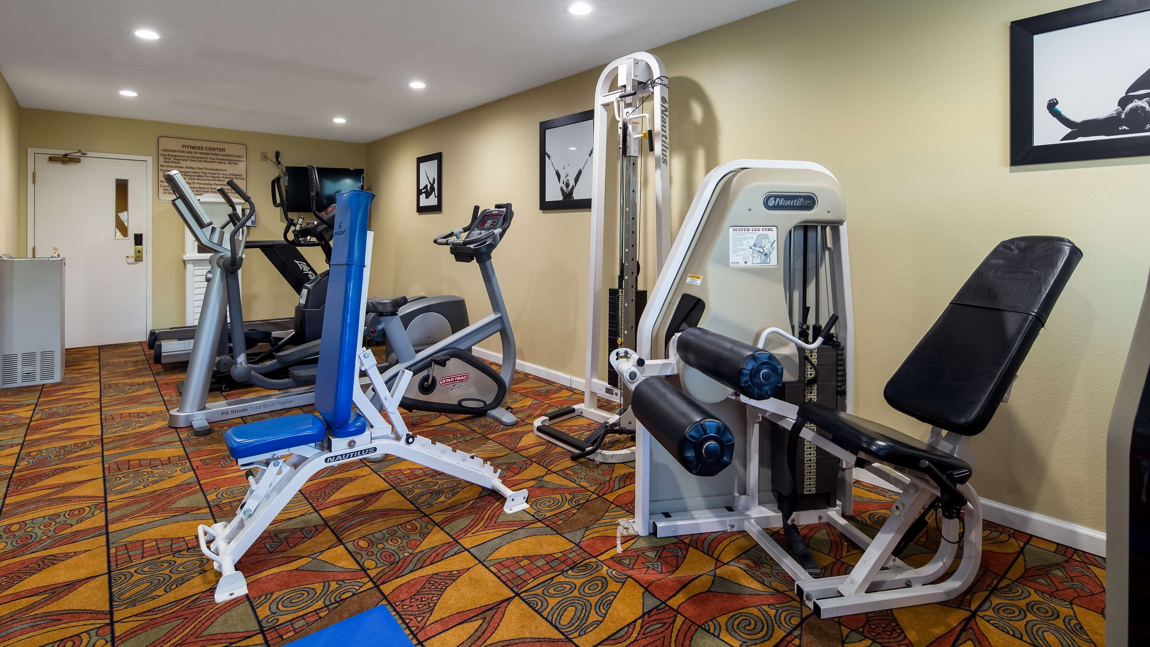 Un gimnasio con diversas máquinas de ejercicio, incluyendo una prensa de piernas Nautilus, una elíptica StarTrac y una cinta de correr.