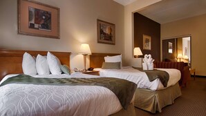 Habitación de hotel con dos camas, una mesita de noche con lámpara, teléfono y un reloj de pared. Se observan cuadros enmarcados en la pared y una silla en la esquina.