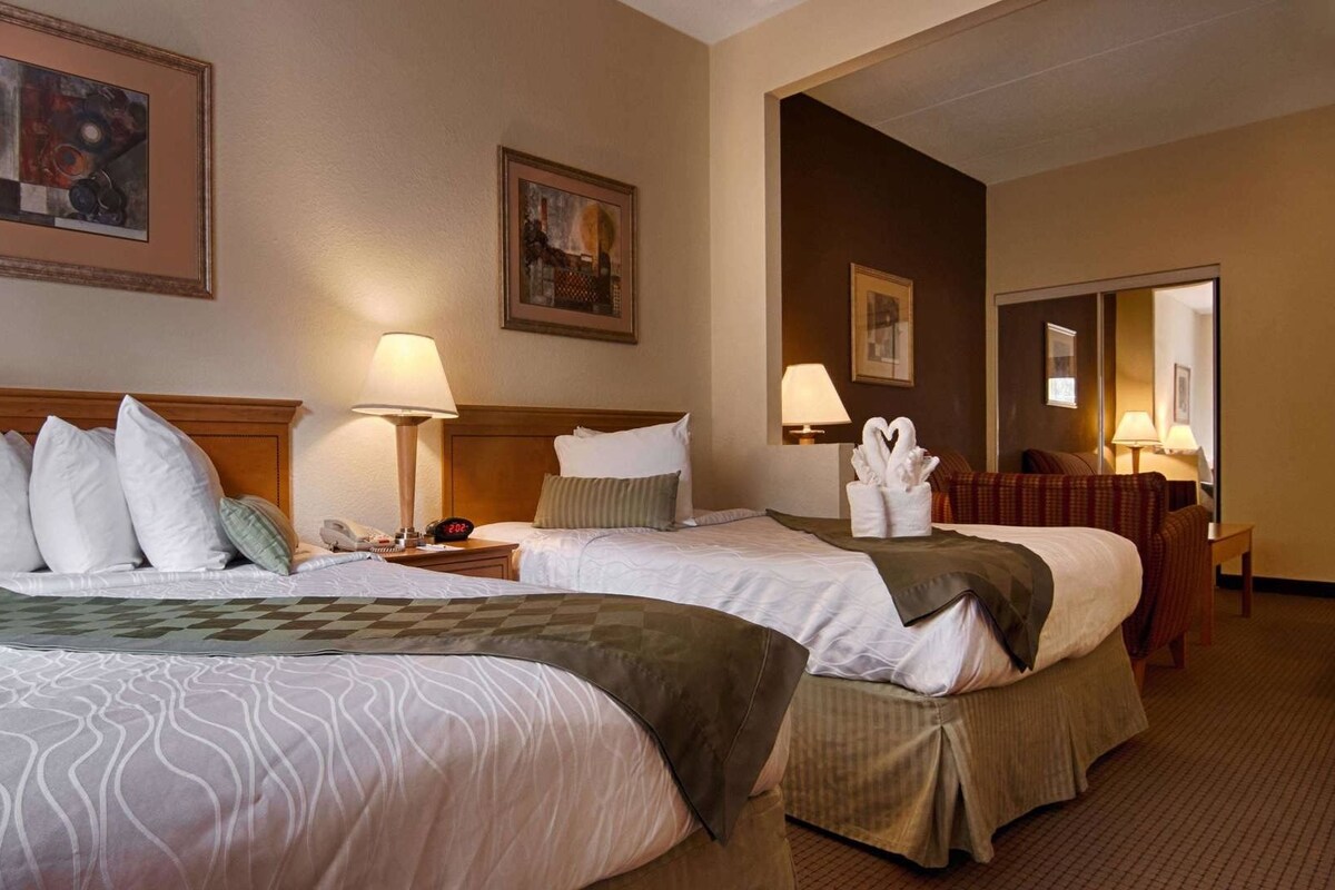 Een hotelkamer met twee bedden, een nachtkastje met een lamp, een telefoon en een aan de muur hangend schilderij.