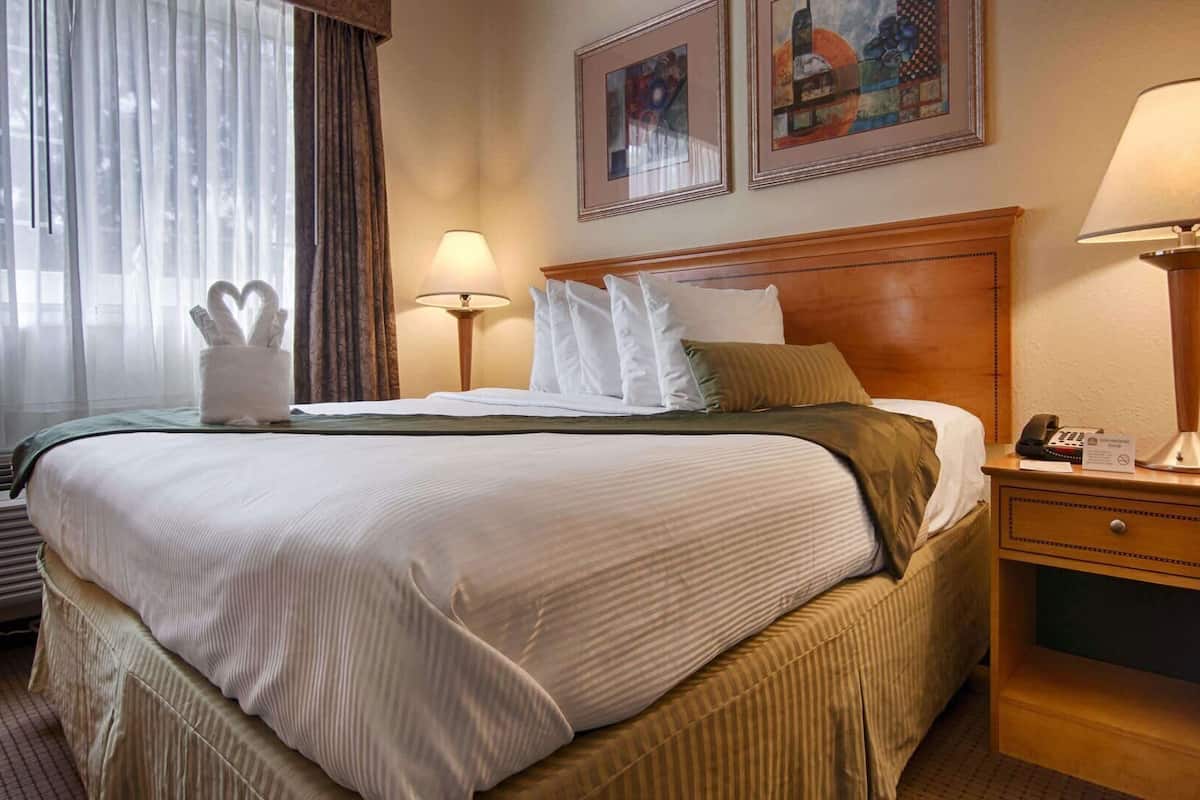 A hotel room with a large bed, two bedside lamps, a nightstand with a phone, and a window with curtains.