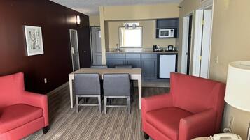 Una habitación de hotel compacta con zona de comedor, kitchenette y dos sillones rojos.