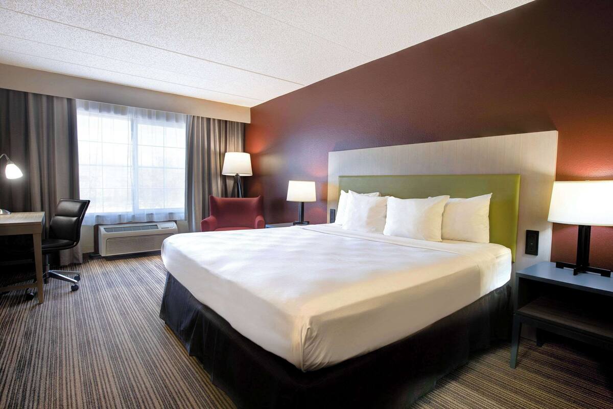 A hotel room with a large bed, a desk, a chair, and a lamp.