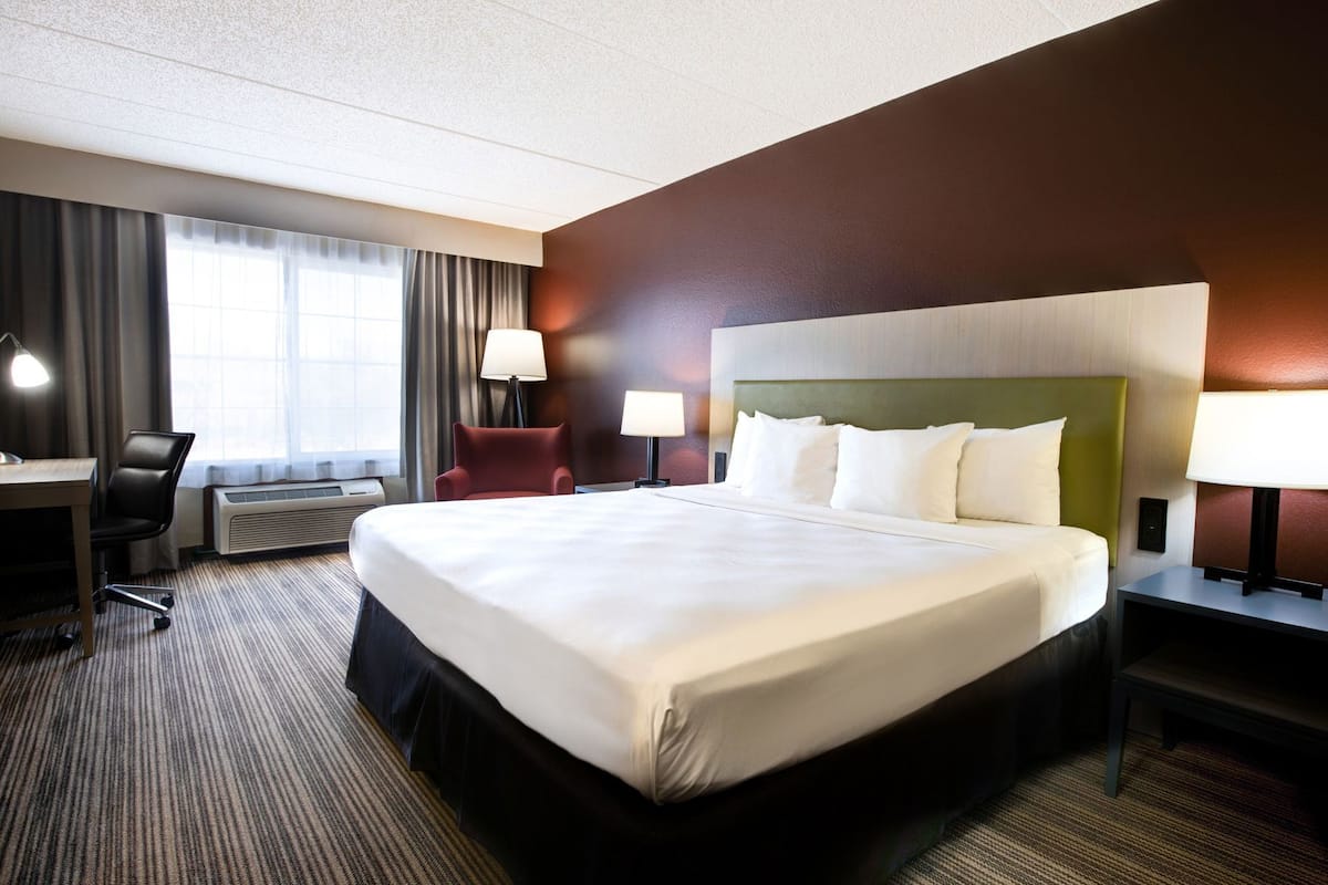 A hotel room with a large bed, a desk, a chair, and a window with curtains.