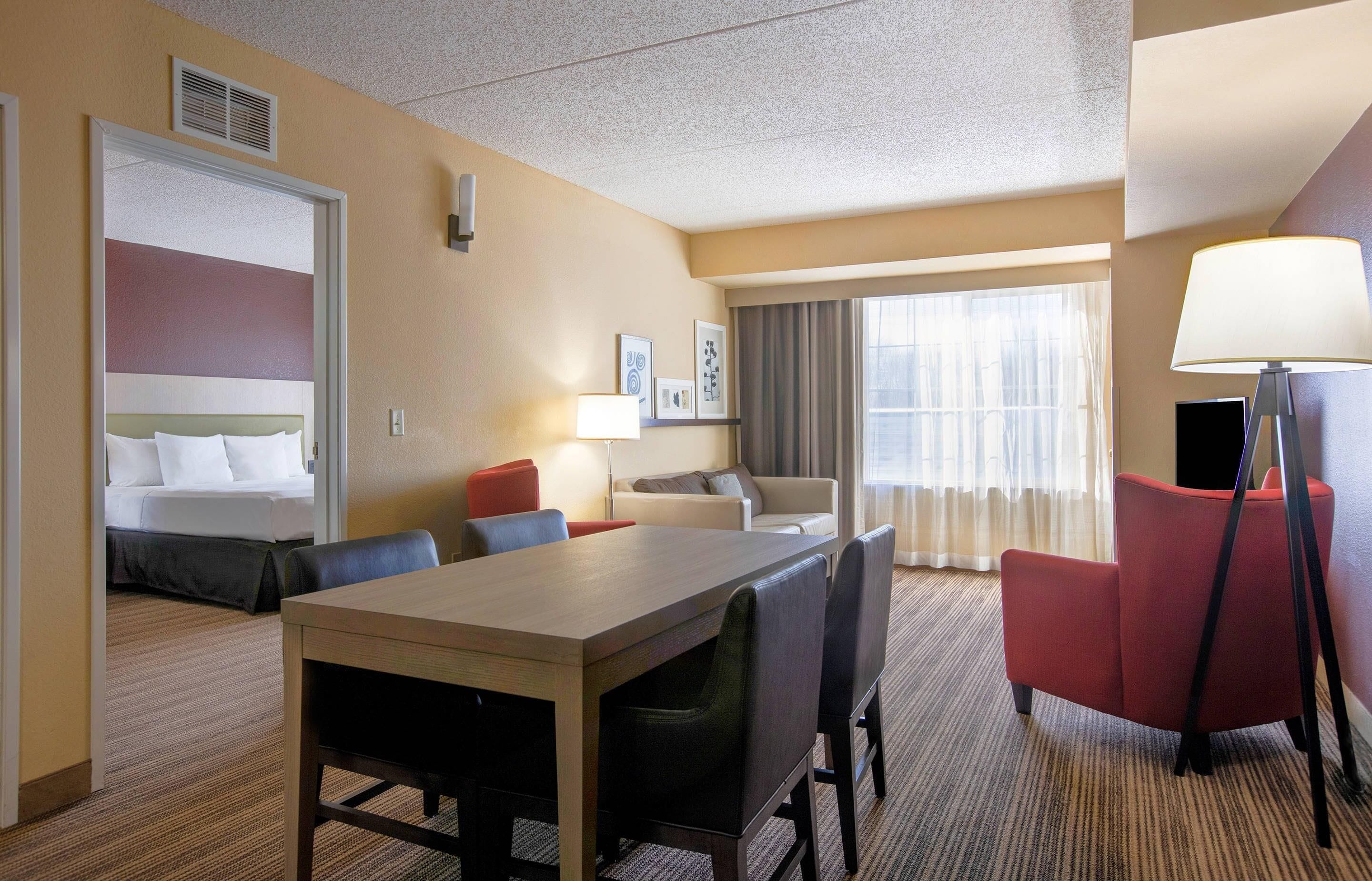 A hotel room with a bed, a desk with chairs, a sofa, a TV, and a lamp.