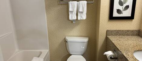 A bathroom with a bathtub, toilet, towel rack, and a framed botanical print on the wall.