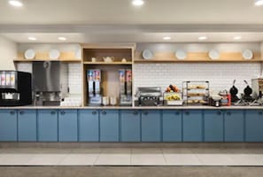 A modern kitchen with blue cabinets, a coffee machine, and various food items on display.