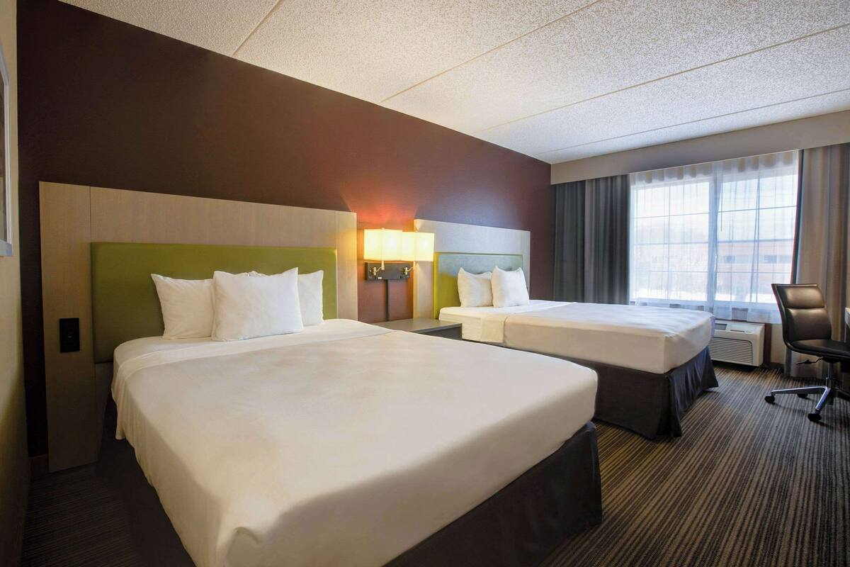A hotel room with two beds, a desk, a chair, and a window with curtains.
