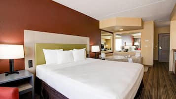 Ein Hotelzimmer mit einem großen Bett, Nachttischlampen, einem Schreibtisch, einem Sessel, einem Badezimmer mit Waschbecken und Spiegel sowie einer Tür.