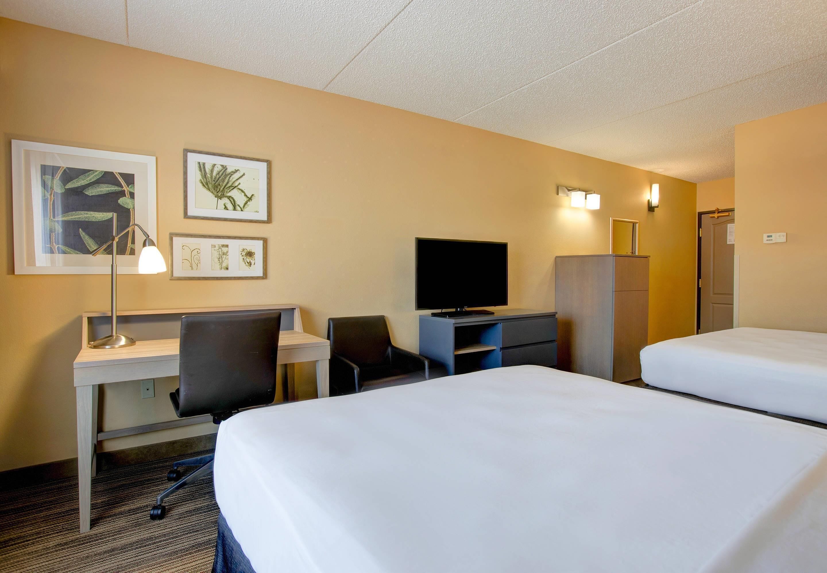 A hotel room with a desk, chair, television, wardrobe, and two beds.