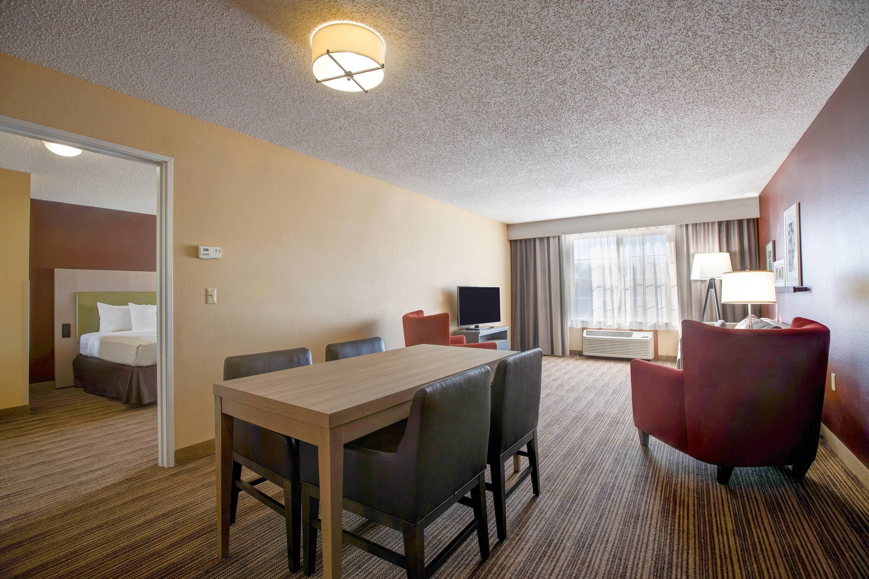 A hotel room with a bed, a desk, a TV, and a dining area.