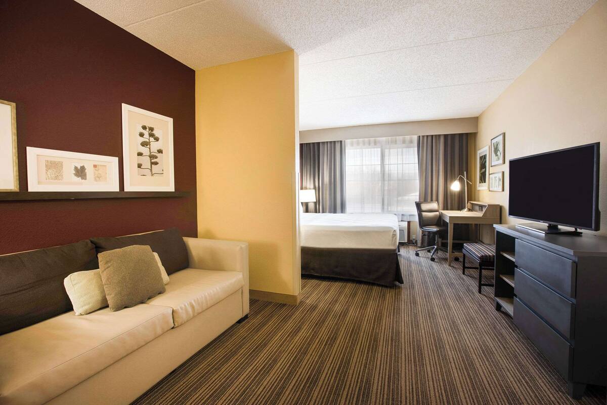 A hotel room with a sofa, a desk, a TV, and framed pictures on the wall.