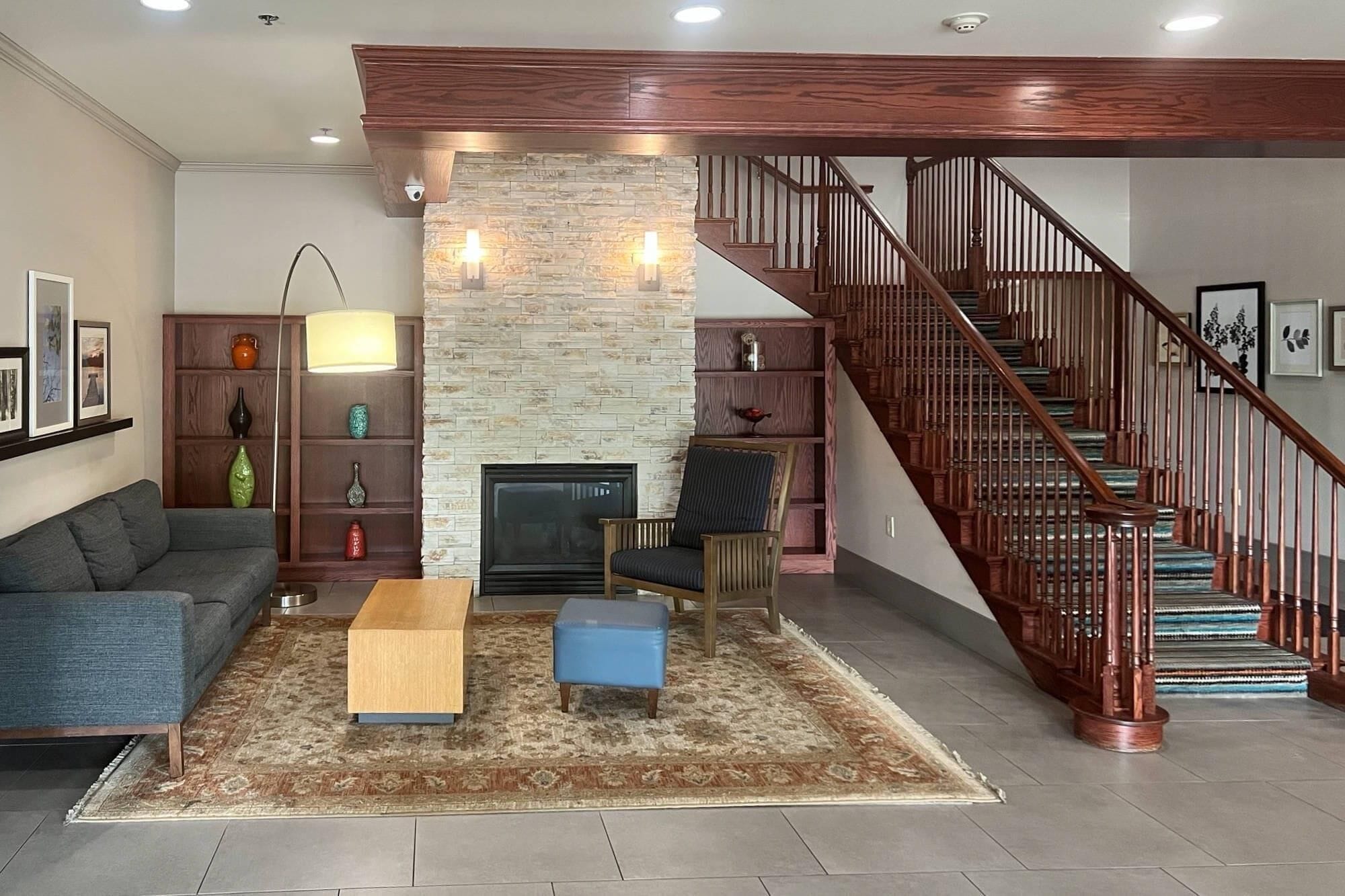Una sala de estar con chimenea de piedra, un sofá, una mesa de centro, una silla y una escalera con barandillas de madera.