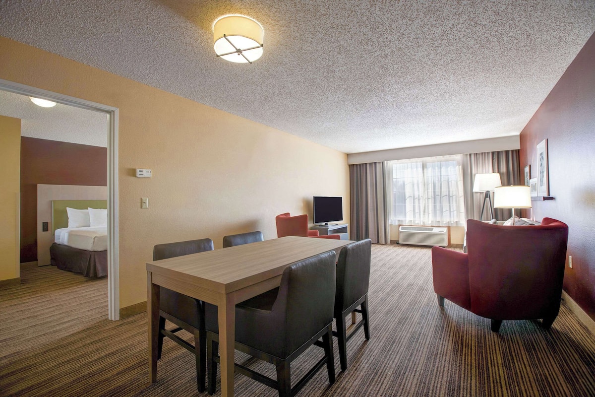 A hotel room with a dining area, a TV, a desk, and a bed.