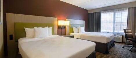 A hotel room with two beds, a desk, a chair, and a window with curtains.
