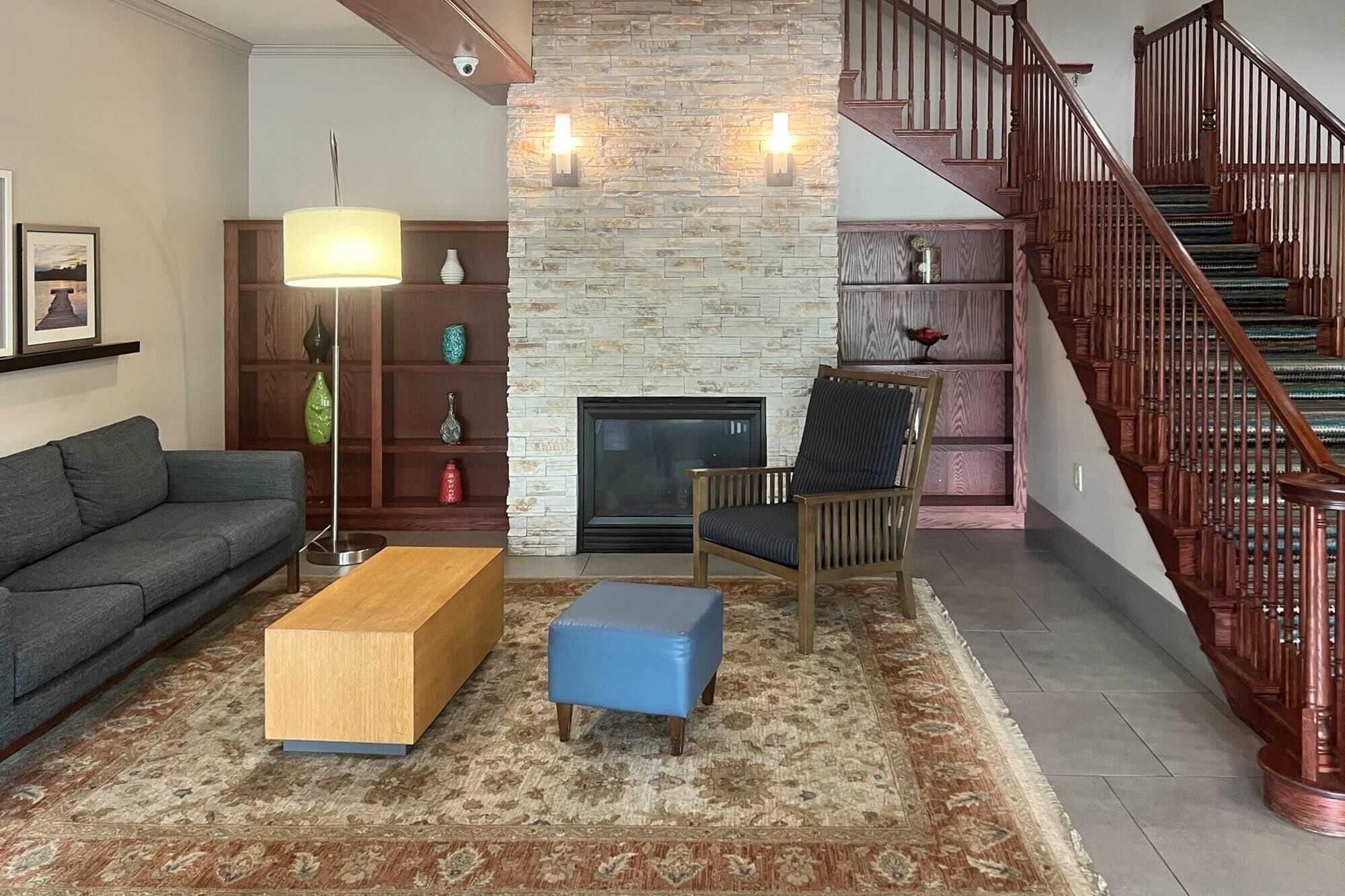 Una sala de estar con chimenea, un sofá, una mesa de centro, un sillón, una estantería y una escalera.