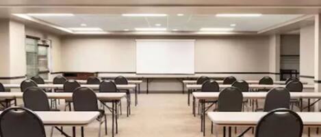 A conference room with rows of tables and chairs, a whiteboard, and a projector screen.