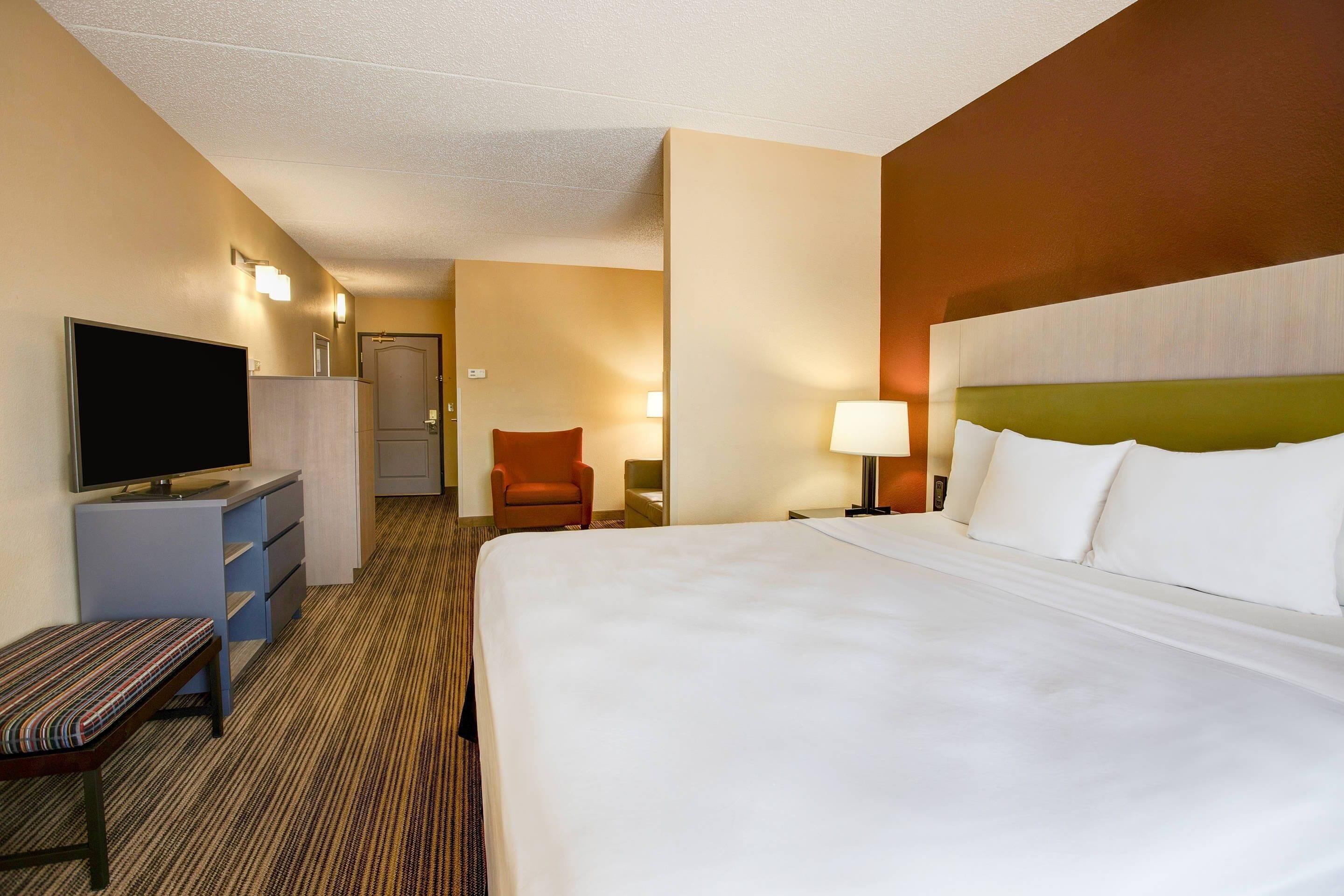 Una habitación de hotel con una cama, televisión, escritorio, silla y lámpara.