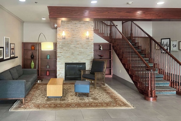 A living room with a stone fireplace, a sofa, a coffee table, and a staircase with wooden railings.