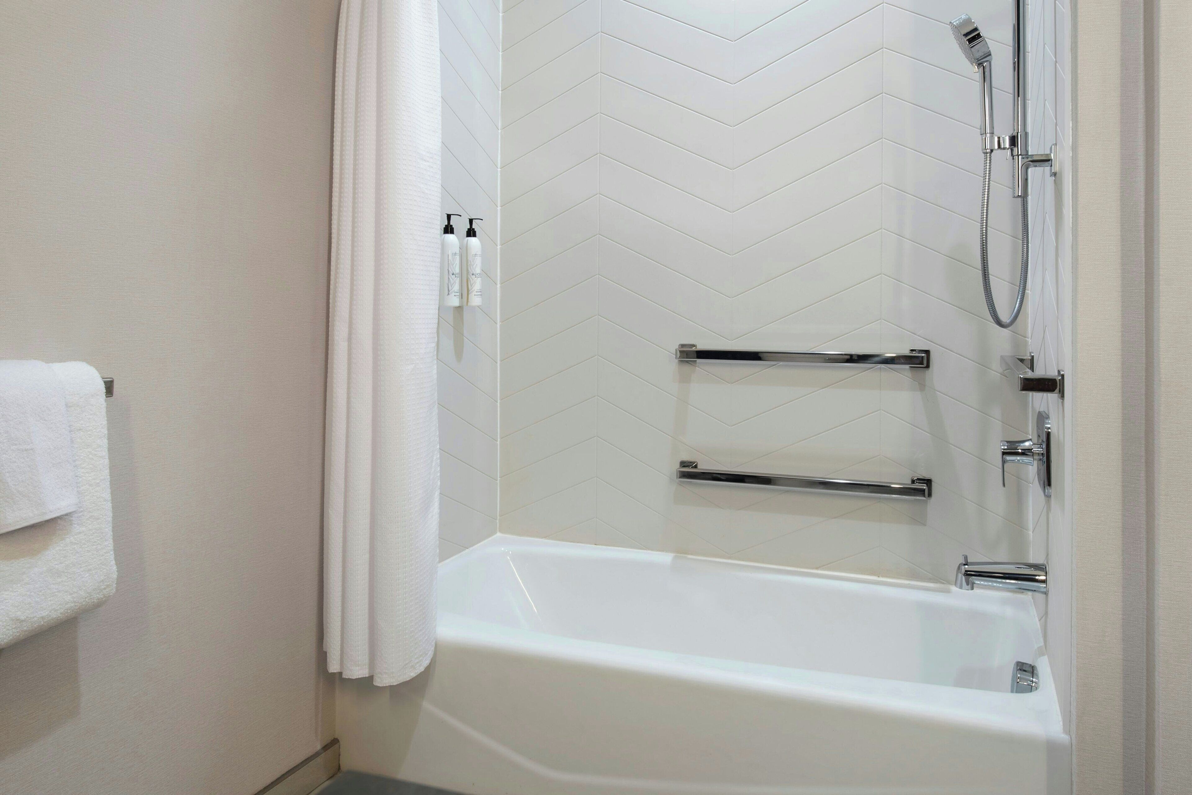Ein modernes Badezimmer mit einer Wand aus weißen Fischgrätplatten, einer weißen Badewanne und einer Dusche mit Duschbrause.
