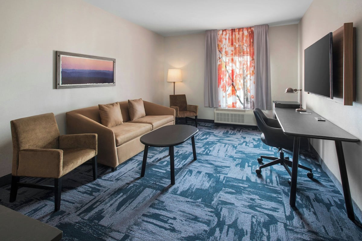 A hotel room with a sofa, armchair, desk, and TV.