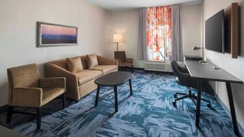 A hotel room with a sofa, armchair, desk, and TV.