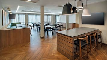 Um hall de hotel moderno com uma ilha central, piso de madeira e uma TV de tela plana na parede.