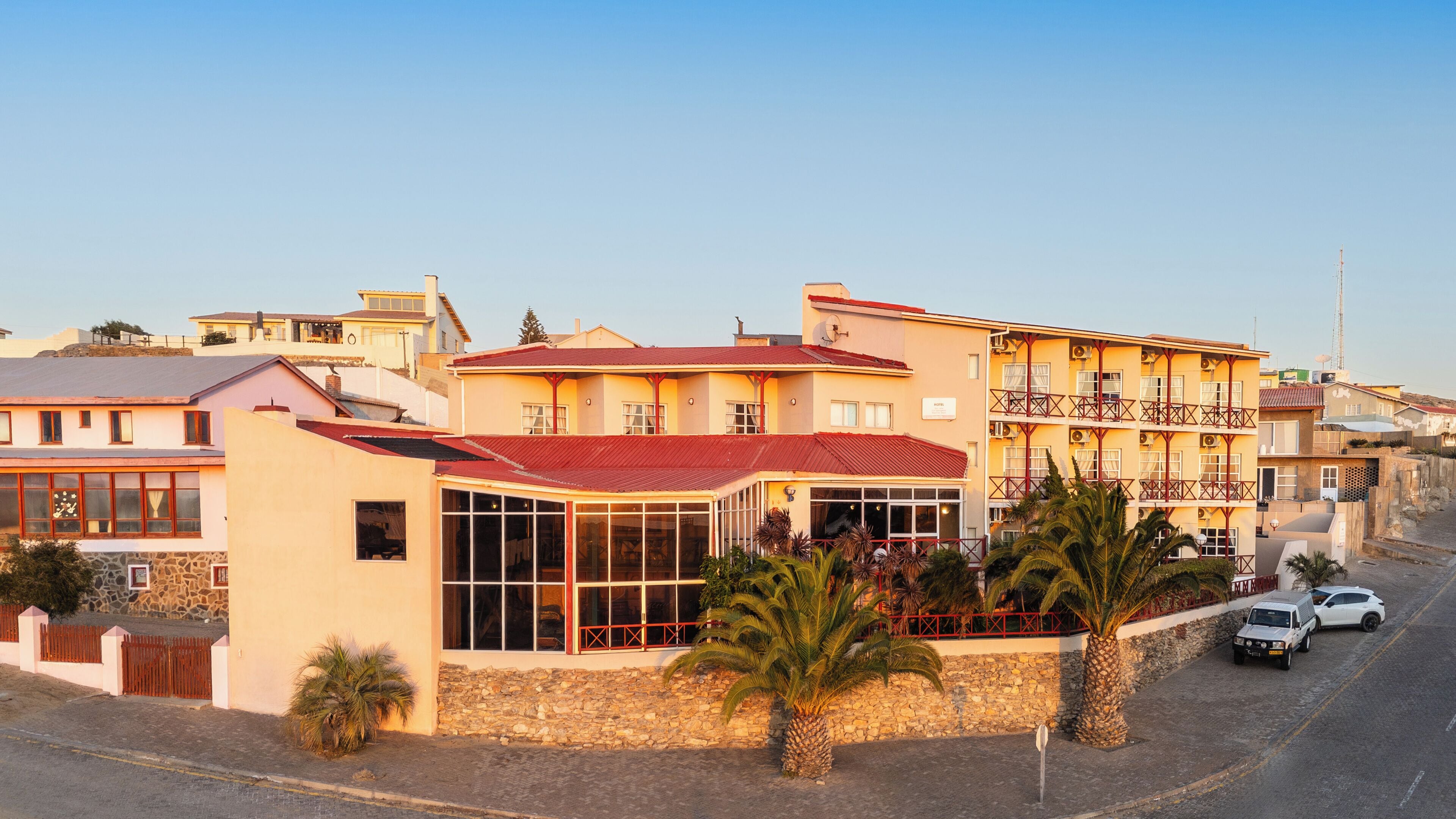 A multi-story hotel with a red roof, large windows, and a stone wall facade.