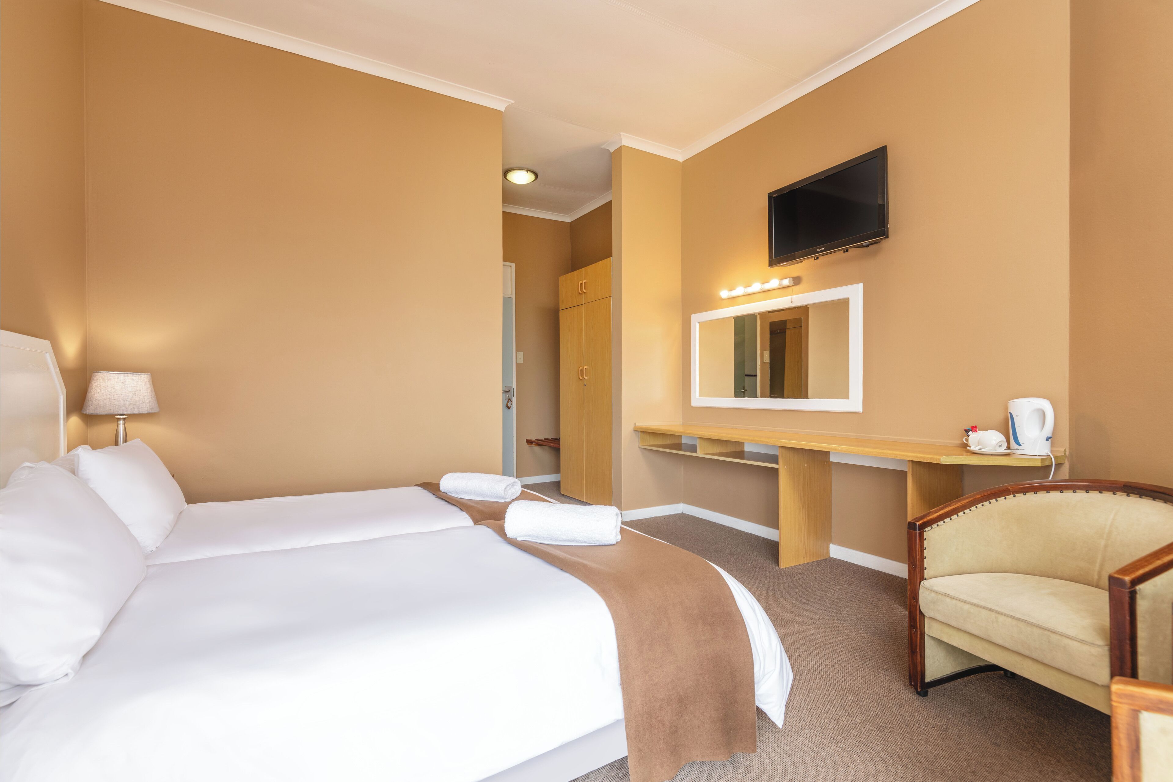 A hotel room with a bed, a chair, a desk with a mirror, and a television.