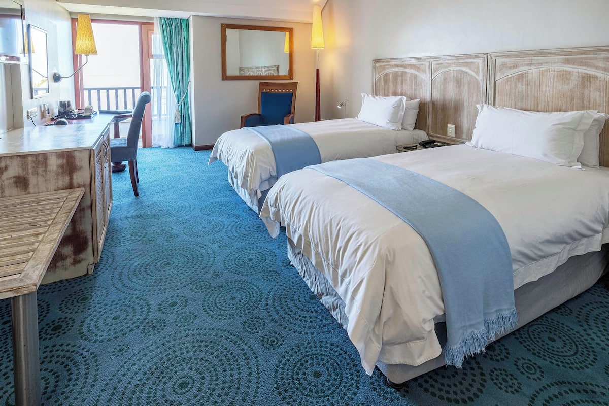 A hotel room with two beds, a desk, and a chair.