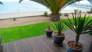A wooden deck with potted plants, a grassy area, and a view of the beach and ocean. - Protea Hotel by Marriott Walvis Bay Pelican Bay (Walvis Bay)