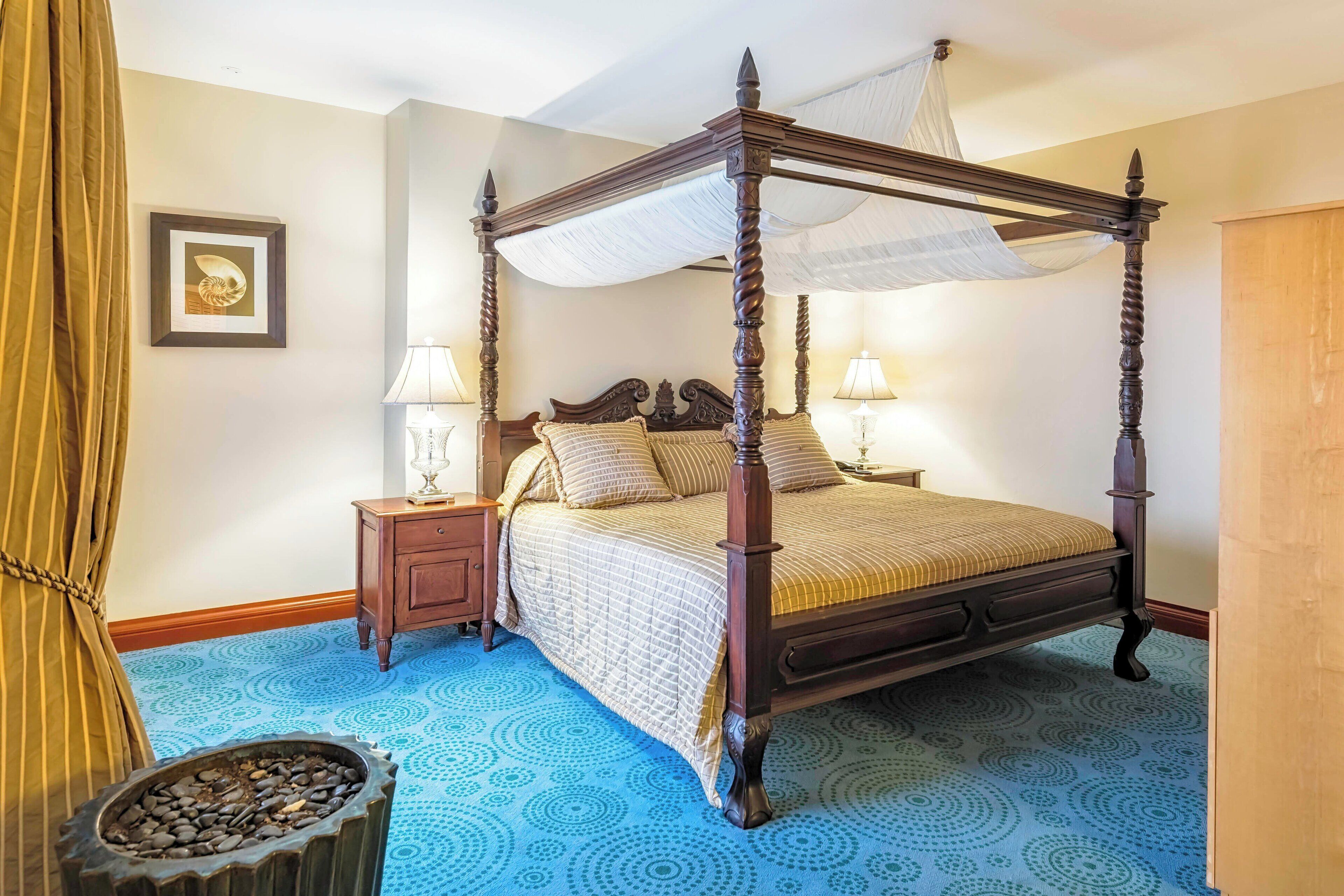 A four-poster bed with a canopy, a nightstand with a lamp, and a decorative bowl on the floor.
