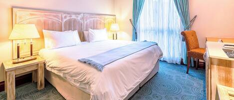 A hotel room with a large bed, two bedside tables with lamps, a chair, and a desk.