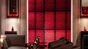 A modern hotel lobby with a patterned red wall, comfortable seating, and a fireplace.