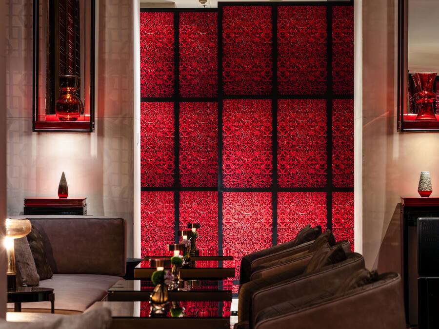 A modern hotel lobby with a patterned red wall, comfortable seating, and a fireplace.