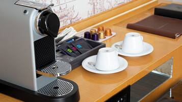 A coffee machine with a tray of coffee cups and a selection of tea bags on a wooden counter.