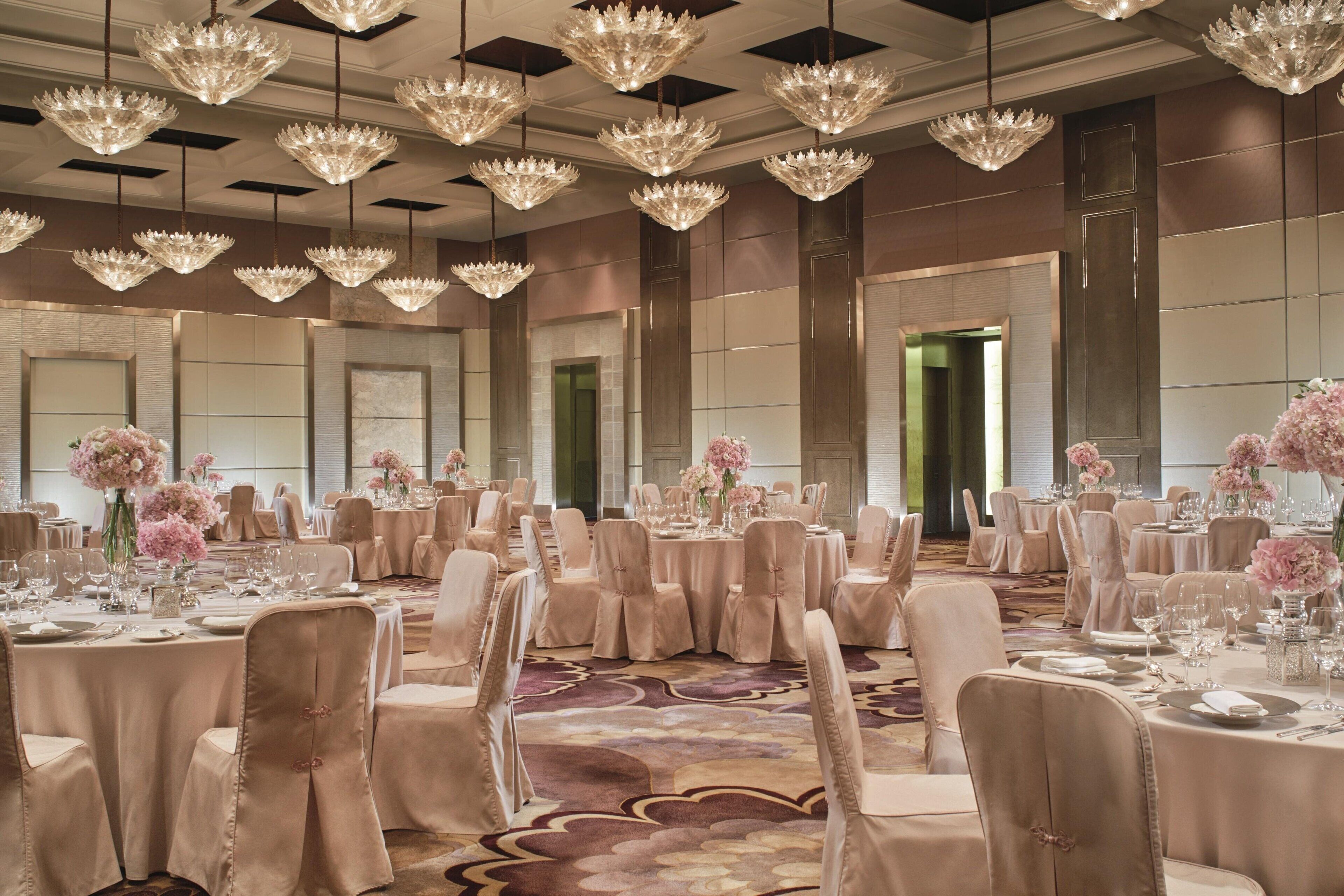 A banquet hall with round tables, chairs, and chandeliers.
