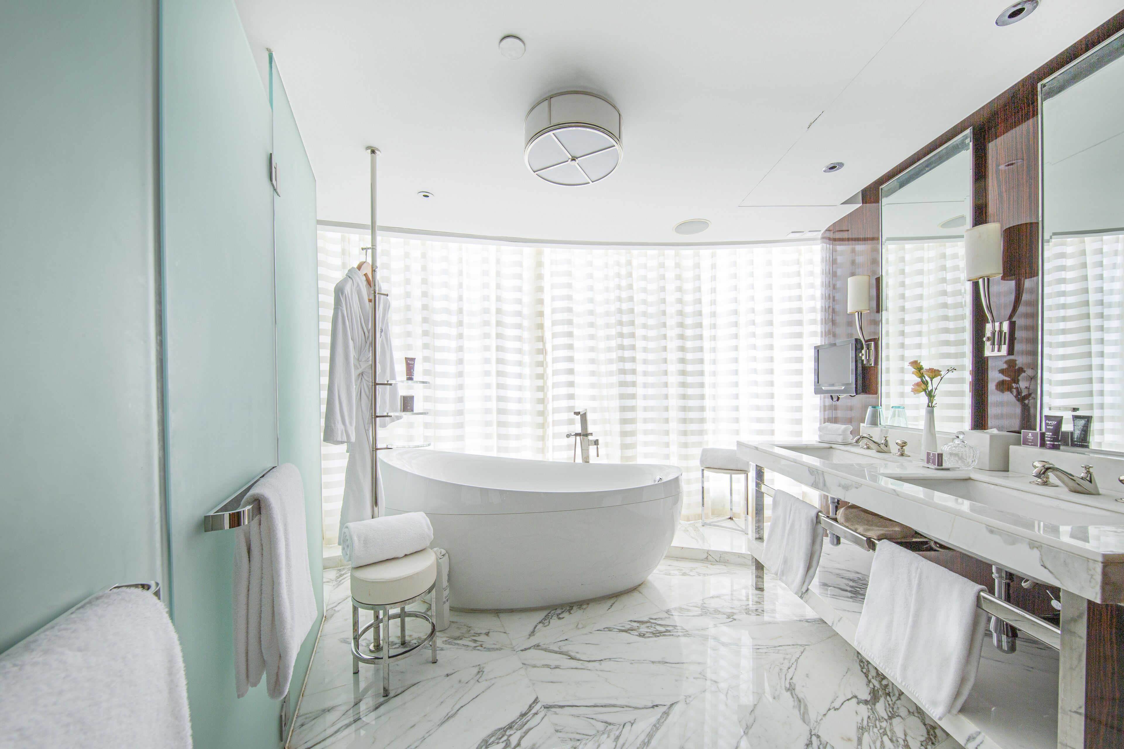 Un baño moderno con una bañera independiente, un tocador espacioso con espejo y una ventana con persianas.
