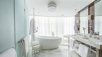 Un baño moderno con una bañera independiente, un tocador espacioso con espejo y una ventana con persianas.