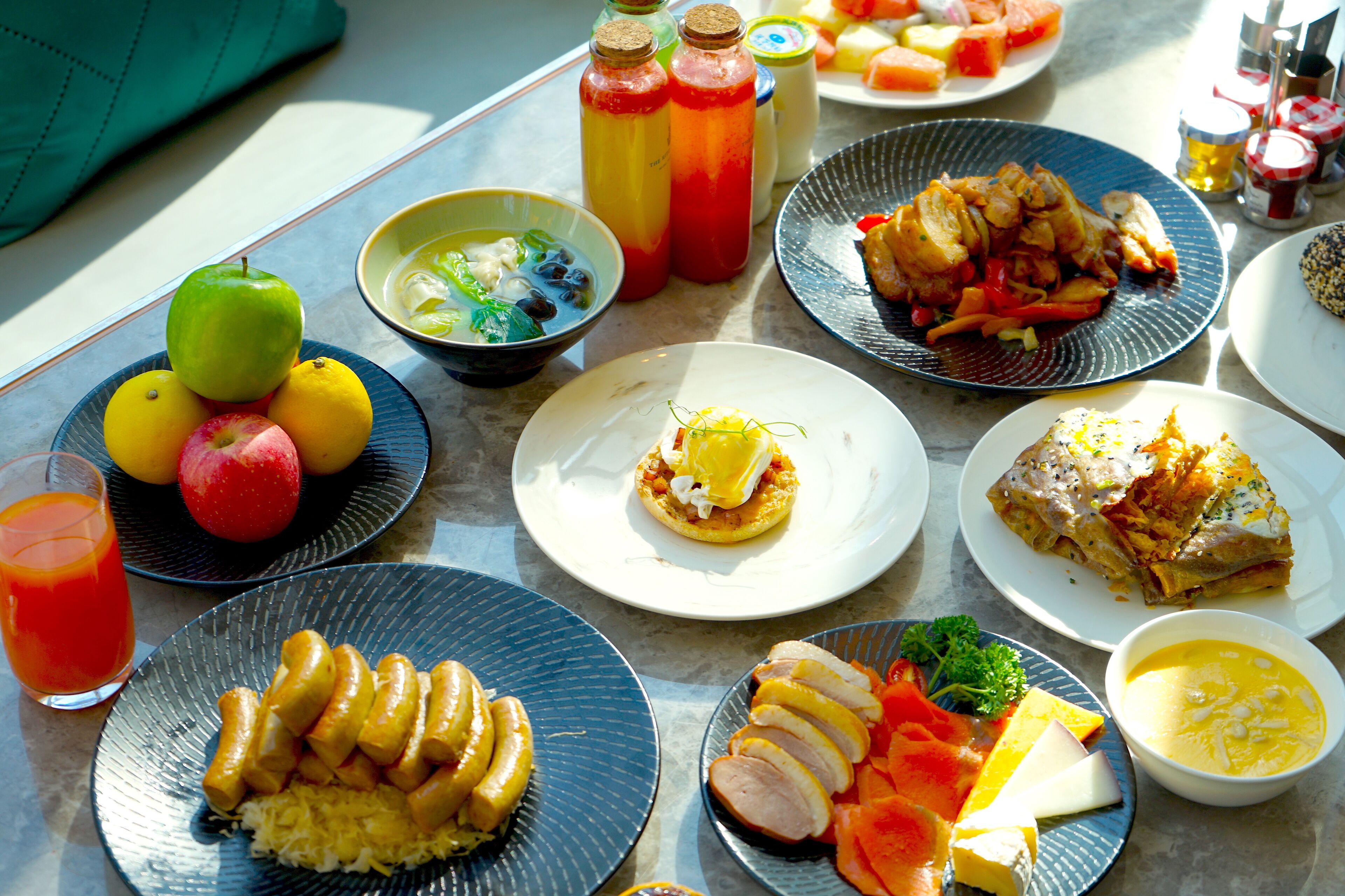 Una mesa con diversos platos, entre ellos frutas, verduras y un vaso de jugo de naranja.